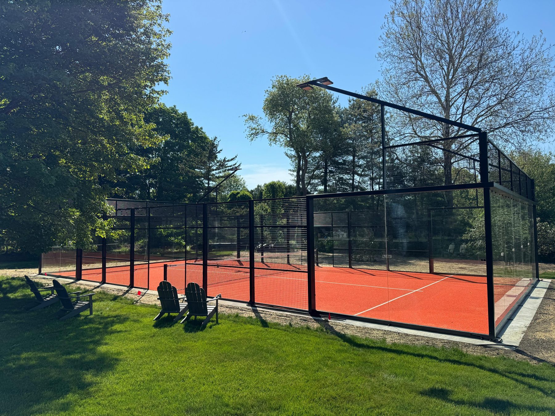 Padel court framed by maple trees with Adirondack chairs