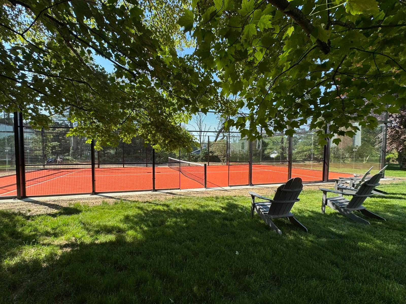 The padel court bathed in sun, glass walls reflecting the New England landscape